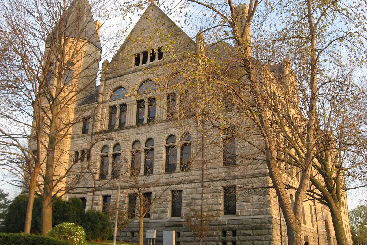The rough-cut stone Wayne County Courthouse in Richmond, with a tall square tower and arched windows, seen through budding spring trees