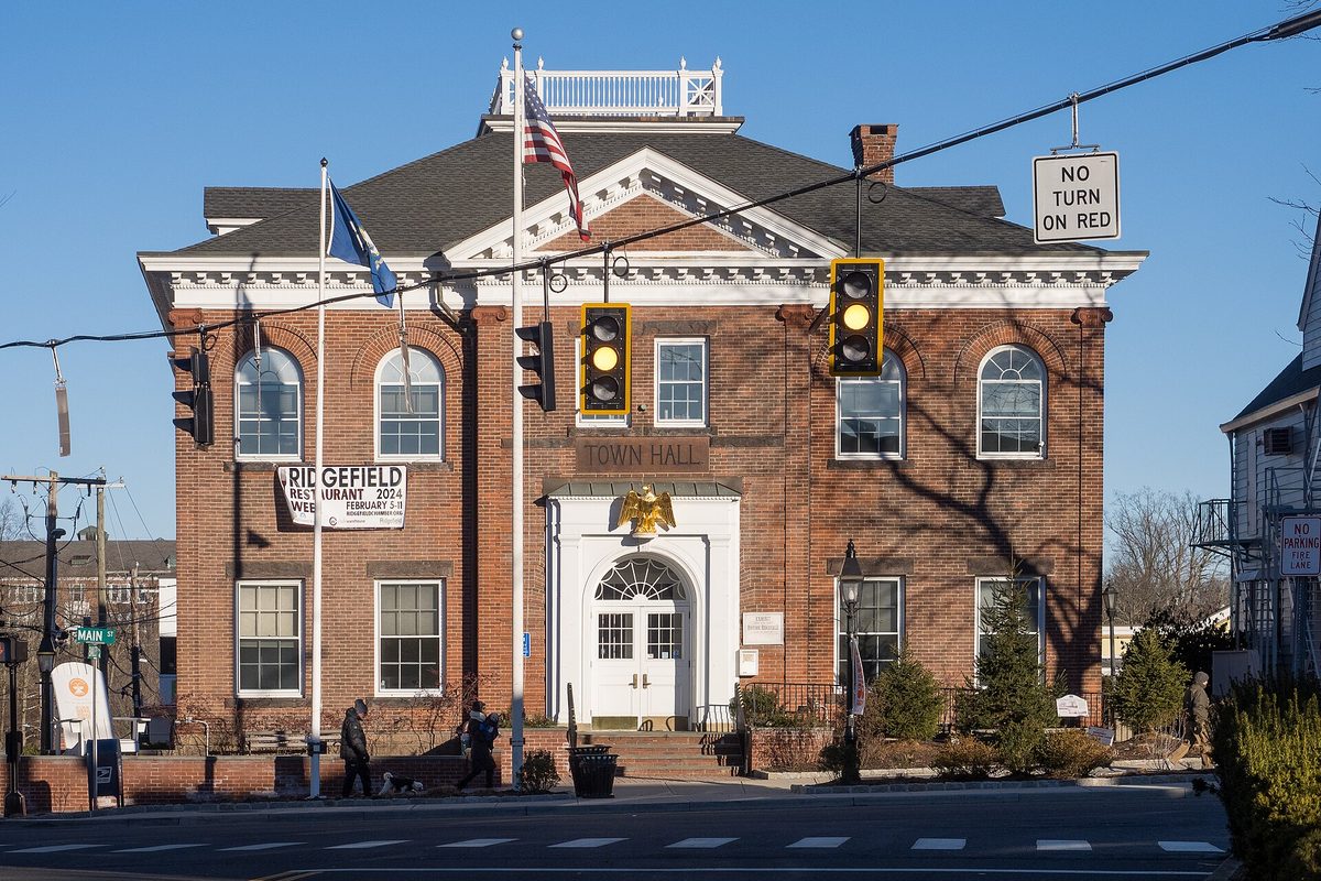 Ridgefield's red-brick Town Hall with white trim and an American flag, seen across the street under a traffic light and a No Turn on Red sign