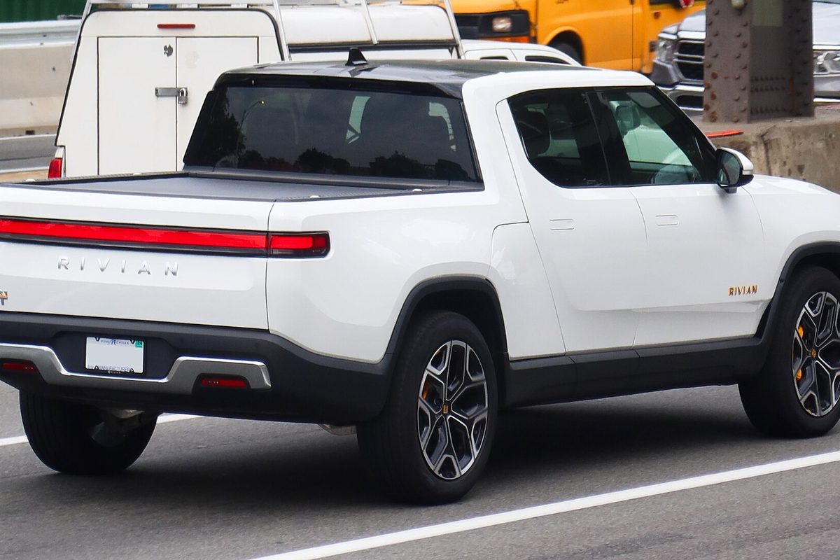 A white 2022 Rivian R1T pickup seen from the rear quarter, driving in traffic in Flushing, Queens, New York