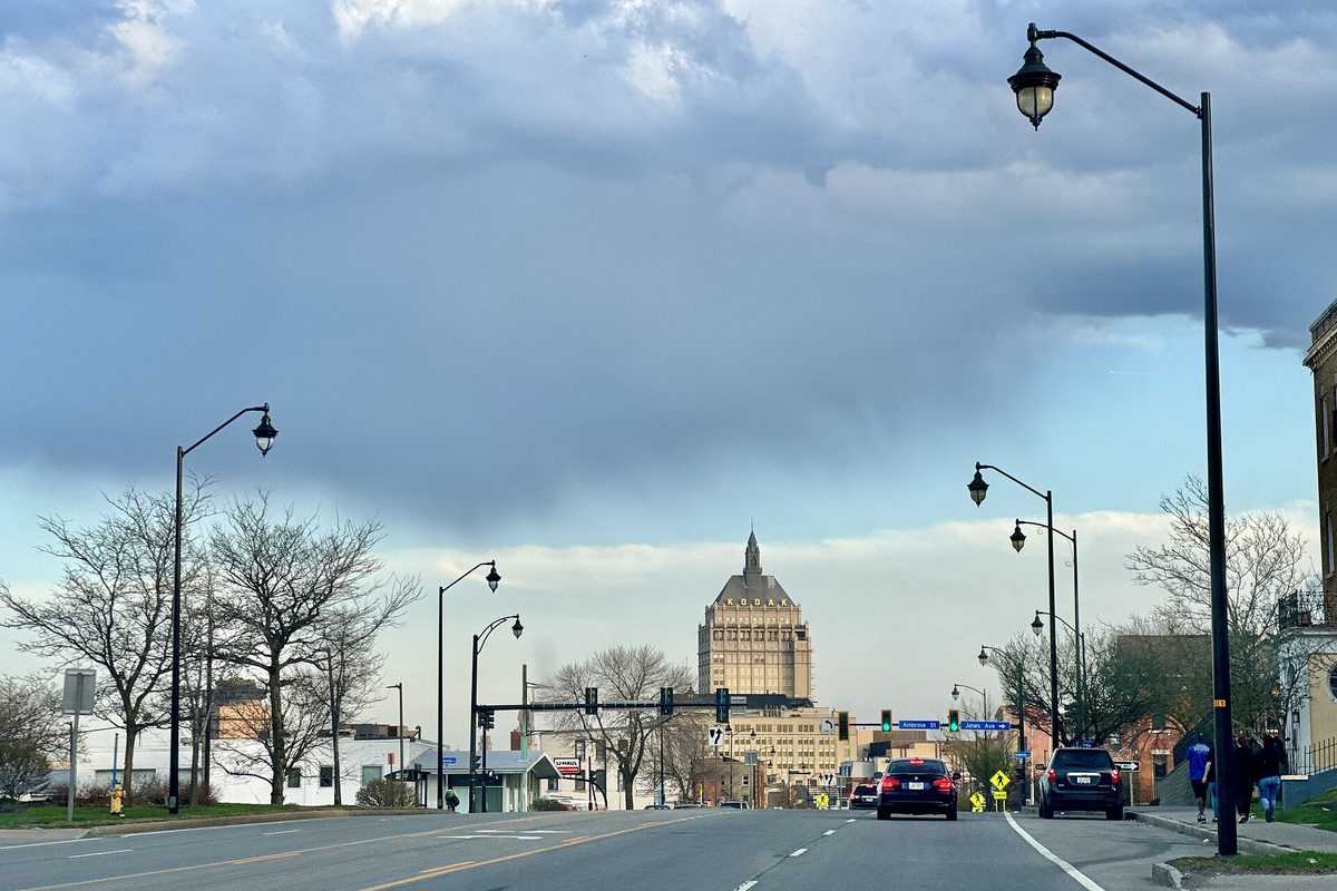 State Street at Brown Square in Rochester under heavy clouds, with old-style street lamps lining the road and the Kodak Tower rising in the distance
