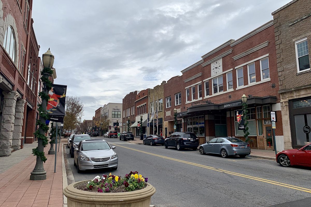 Main Street in downtown Rock Hill, with brick storefronts, a clock on one facade, parked cars at the curb and a planter of flowers beside a lamp post