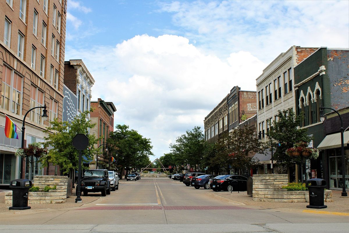 Second Avenue in downtown Rock Island, a street of brick and stone storefronts with planters, lamp posts and parked cars under a partly cloudy sky