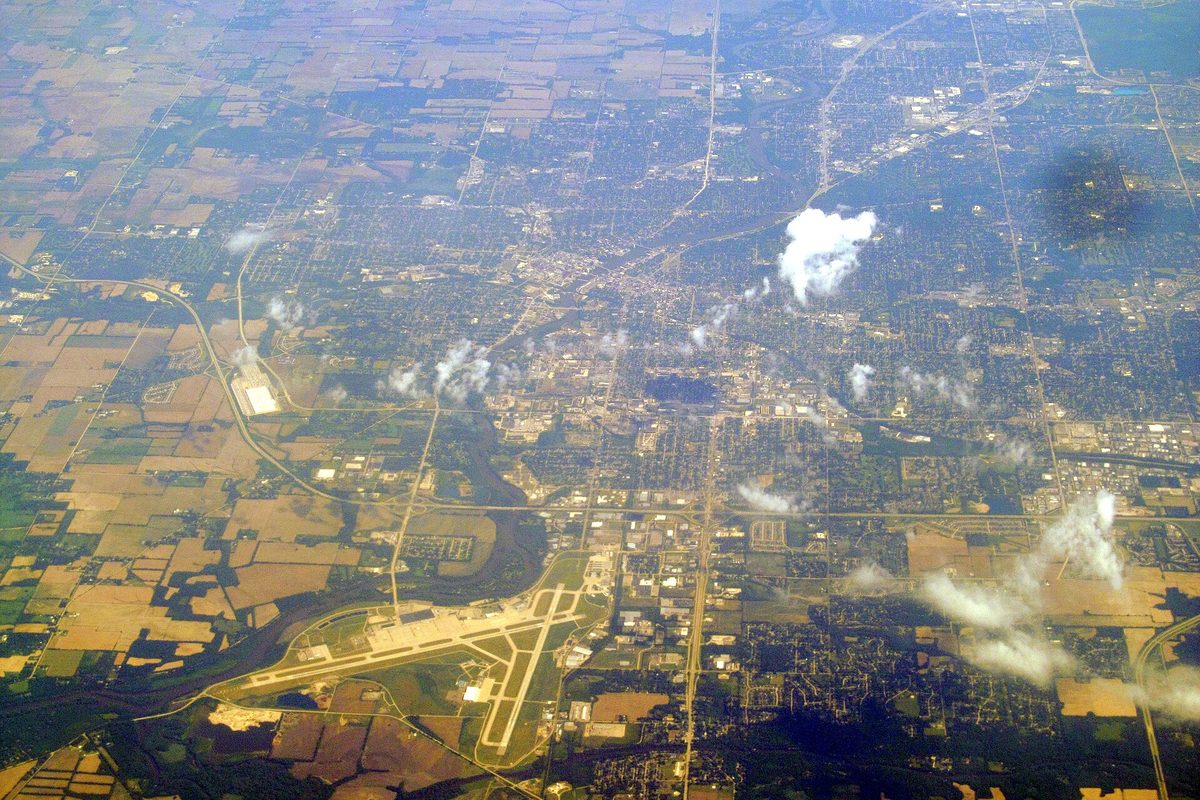 Aerial view of Rockford from high above, with farm fields, a river winding through the city and an airport's crossing runways in the foreground