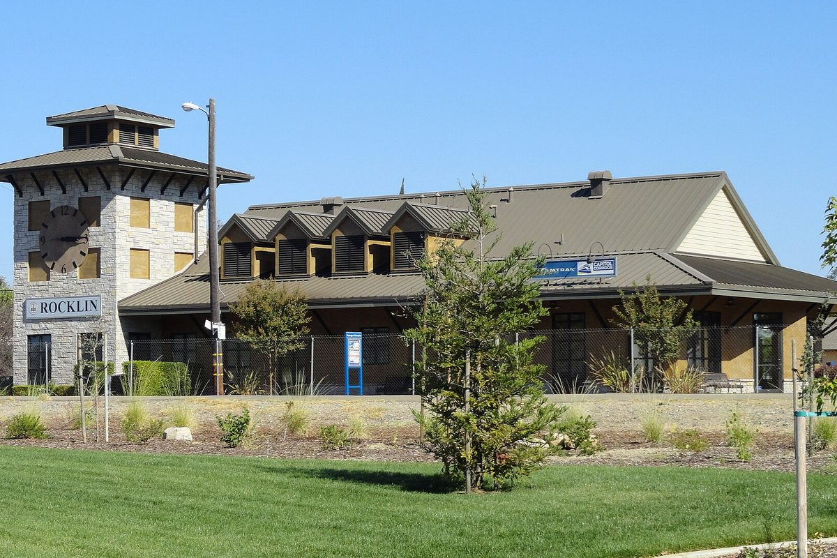 Rocklin's Amtrak station and Chamber of Commerce building, with a stone clock tower, a ROCKLIN sign and a green lawn in front