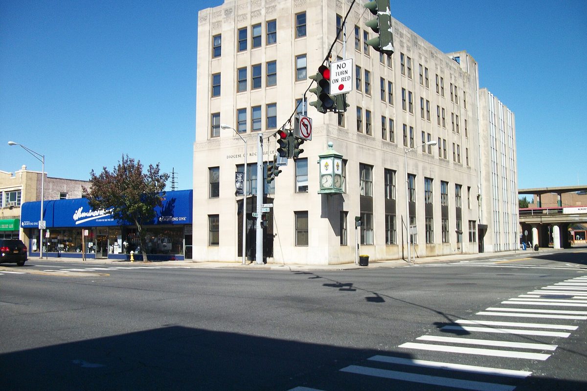 The pale stone office tower of the Diocese of Rockville Centre at Sunrise Highway and North Park Avenue, with traffic lights and a crosswalk in the foreground