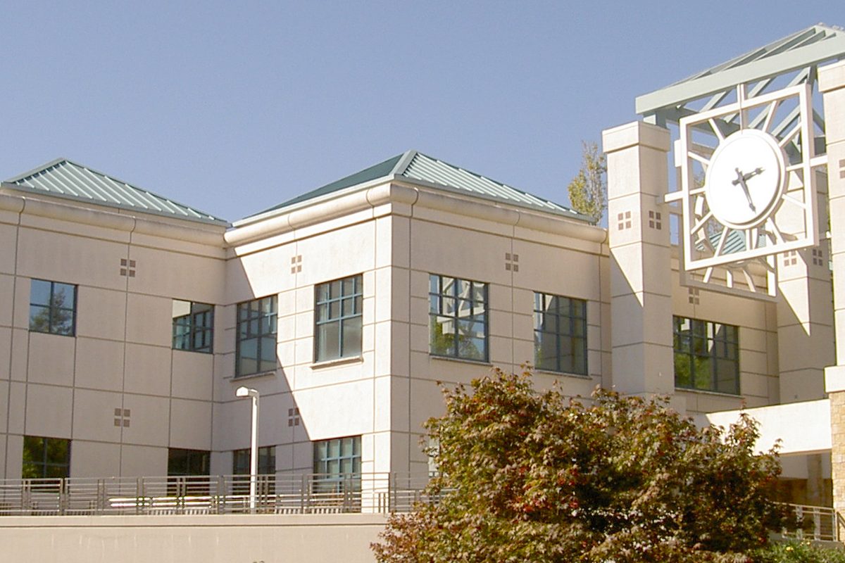 The pale stone Schultz Library at Sonoma State University in Rohnert Park, with a large open-frame clock tower and green roofs under a clear blue sky