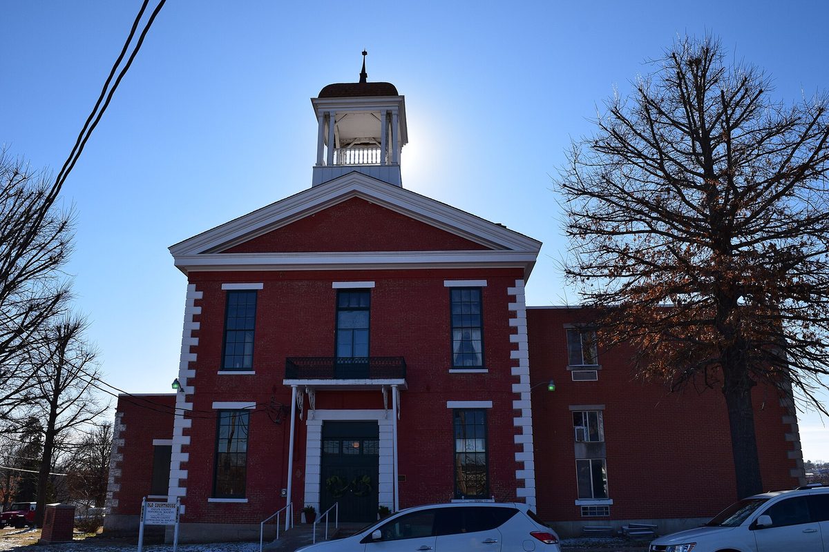 The Old Phelps County Courthouse in Rolla, a red brick building with white trim and a white cupola, beside a bare tree with a white car parked in front