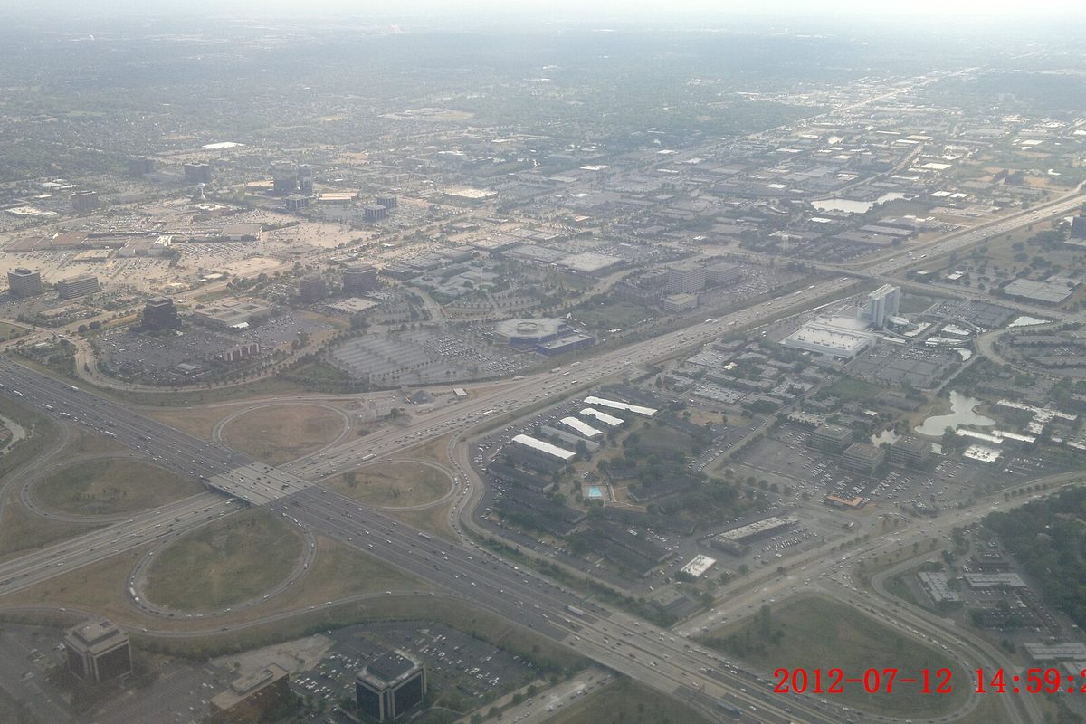 Aerial view over Rolling Meadows showing a cloverleaf highway interchange, office buildings and large parking lots stretching to a hazy horizon