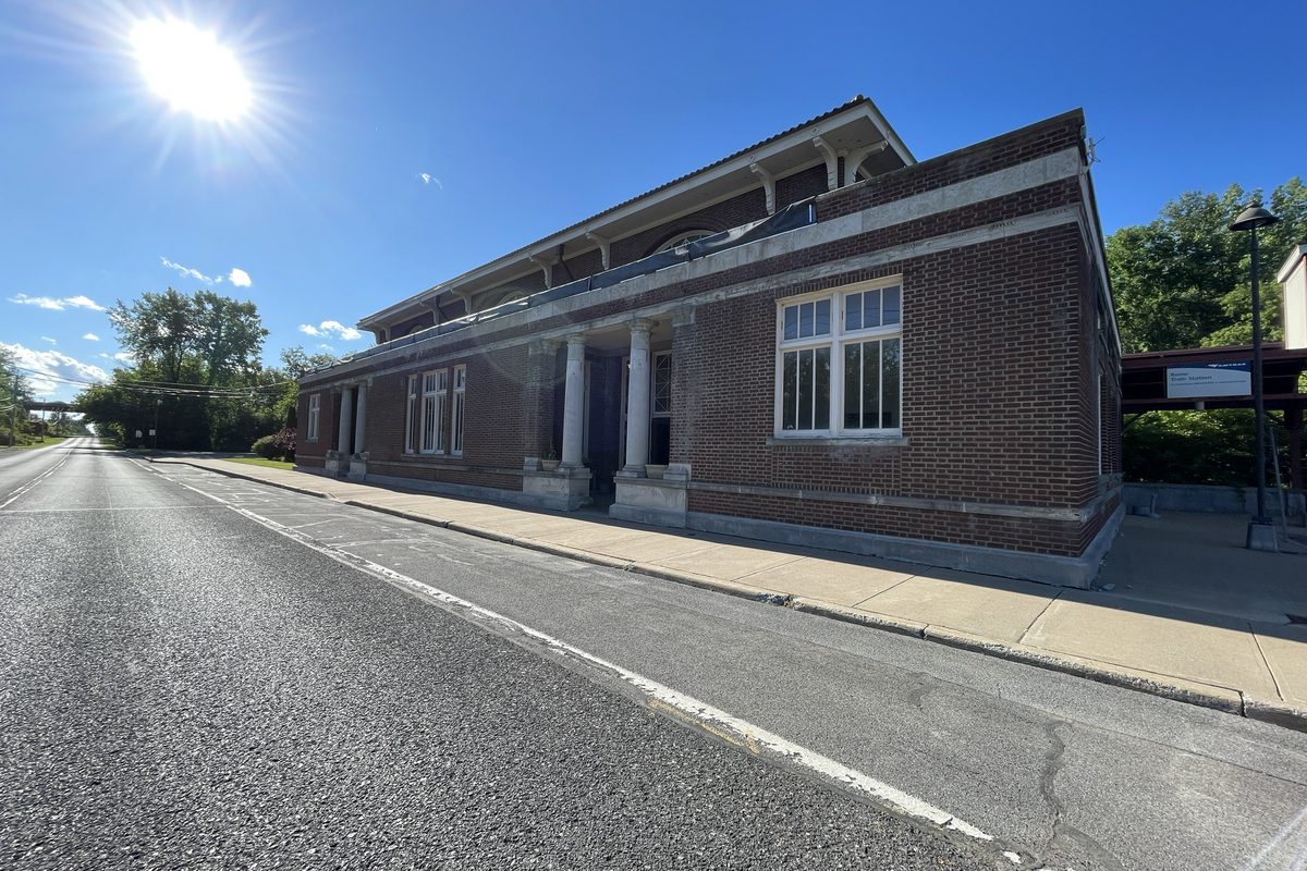 The brick Rome train station with white columns and tall windows beside an empty road on a bright, sunny day