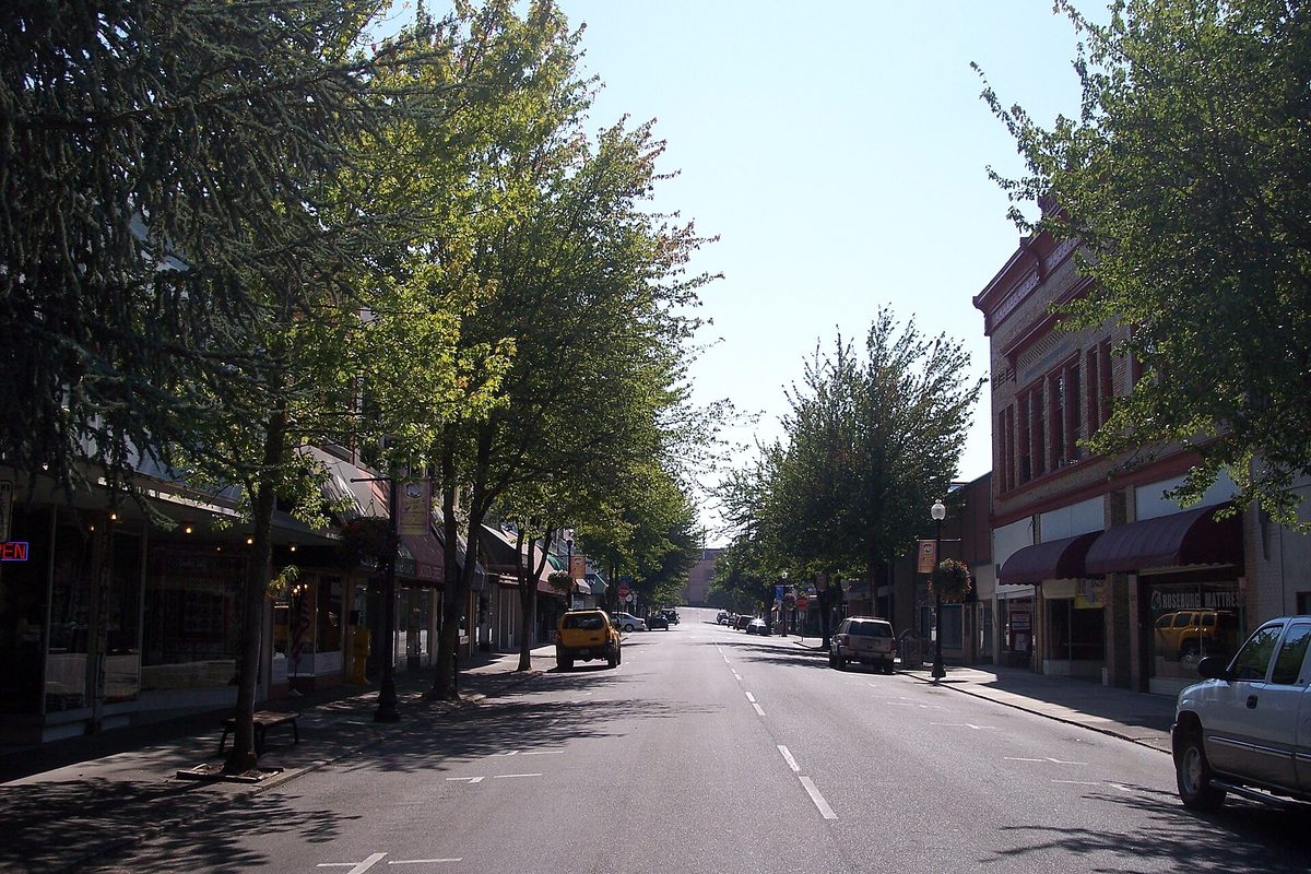 SE Jackson Street in downtown Roseburg, lined with leafy trees and brick storefronts on a sunny day