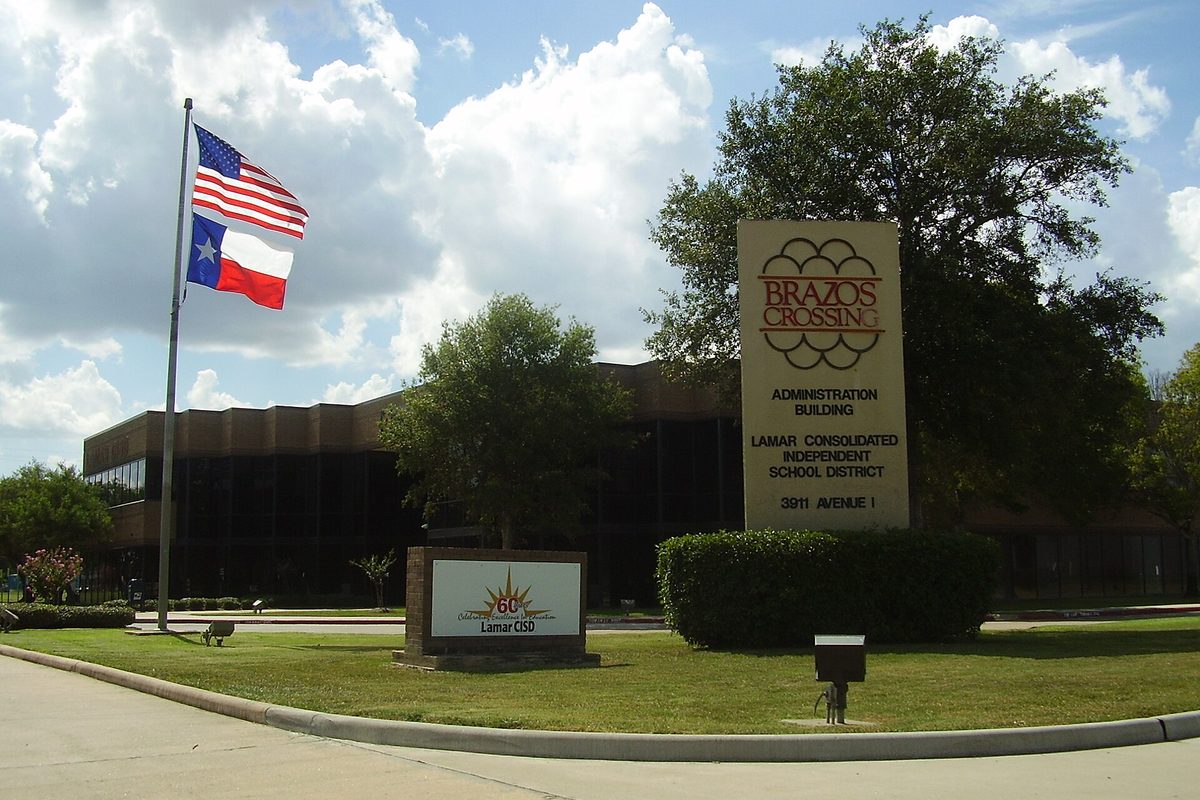 The Brazos Crossing sign outside the Lamar Consolidated school district administration building in Rosenberg, with U.S. and Texas flags and a green lawn