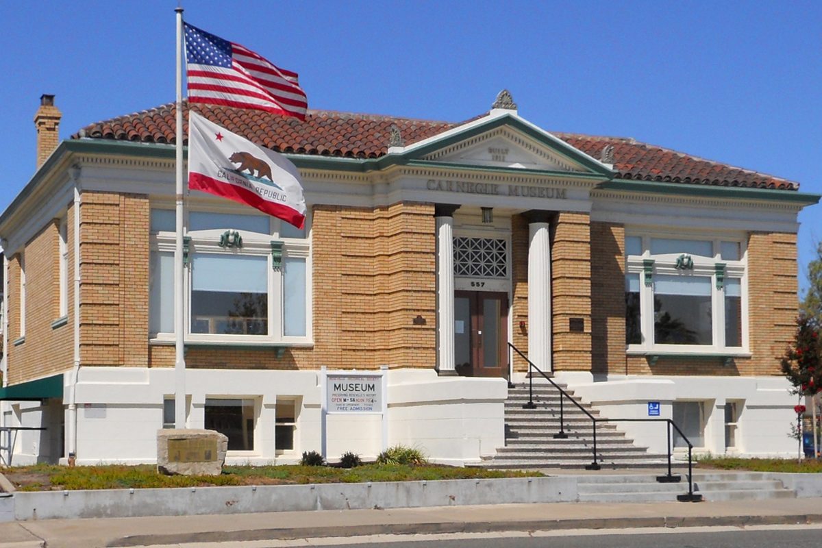 The tan brick Carnegie Library building in Roseville, now a museum, with US and California flags flying out front under a clear blue sky