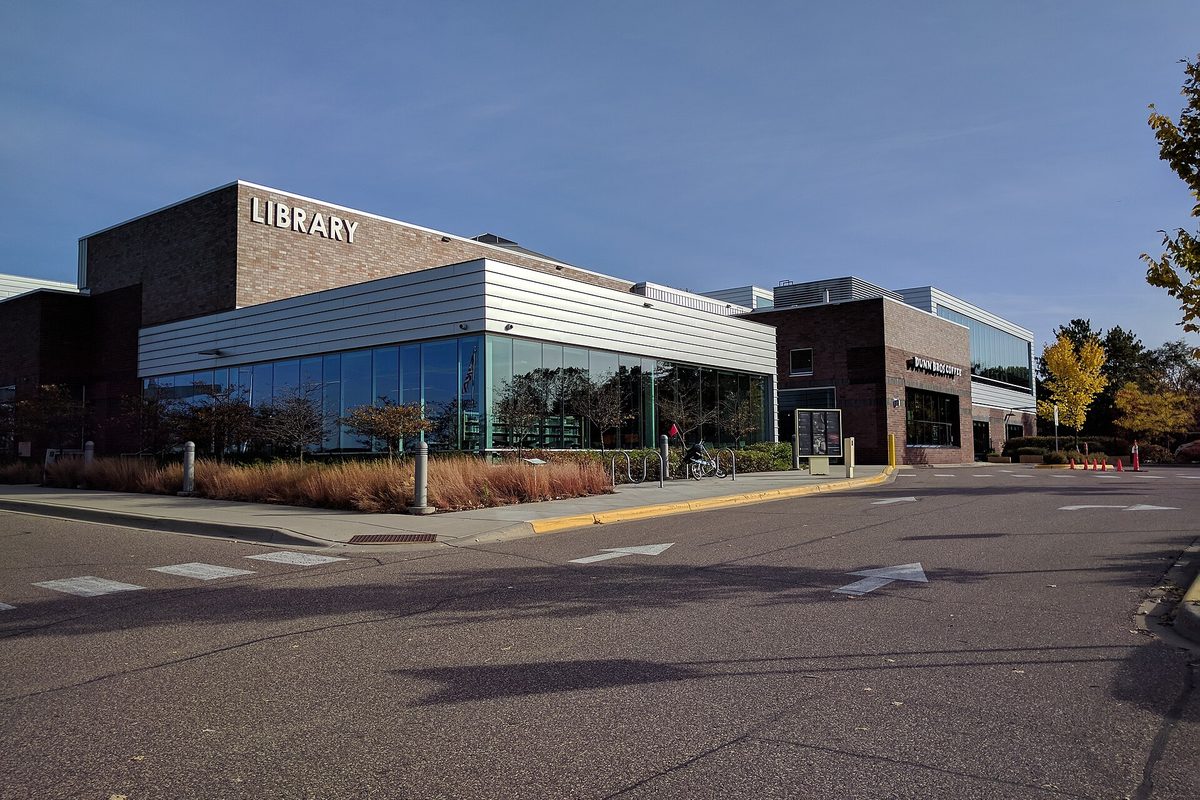 The Roseville library, a long brick and white-paneled building with LIBRARY in large letters and a wall of glass windows, beside an empty parking lot