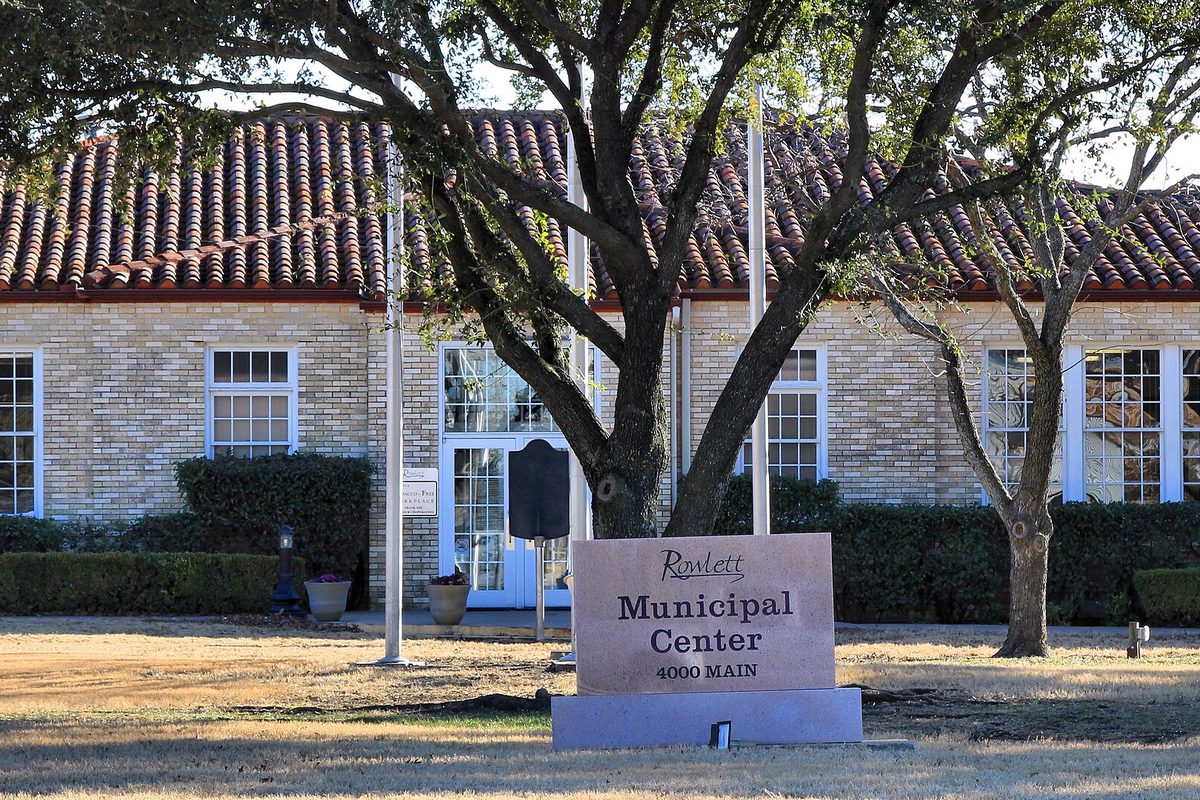 The Rowlett Municipal Center at 4000 Main, a tan brick building with a red tile roof behind a stone sign and a large oak tree