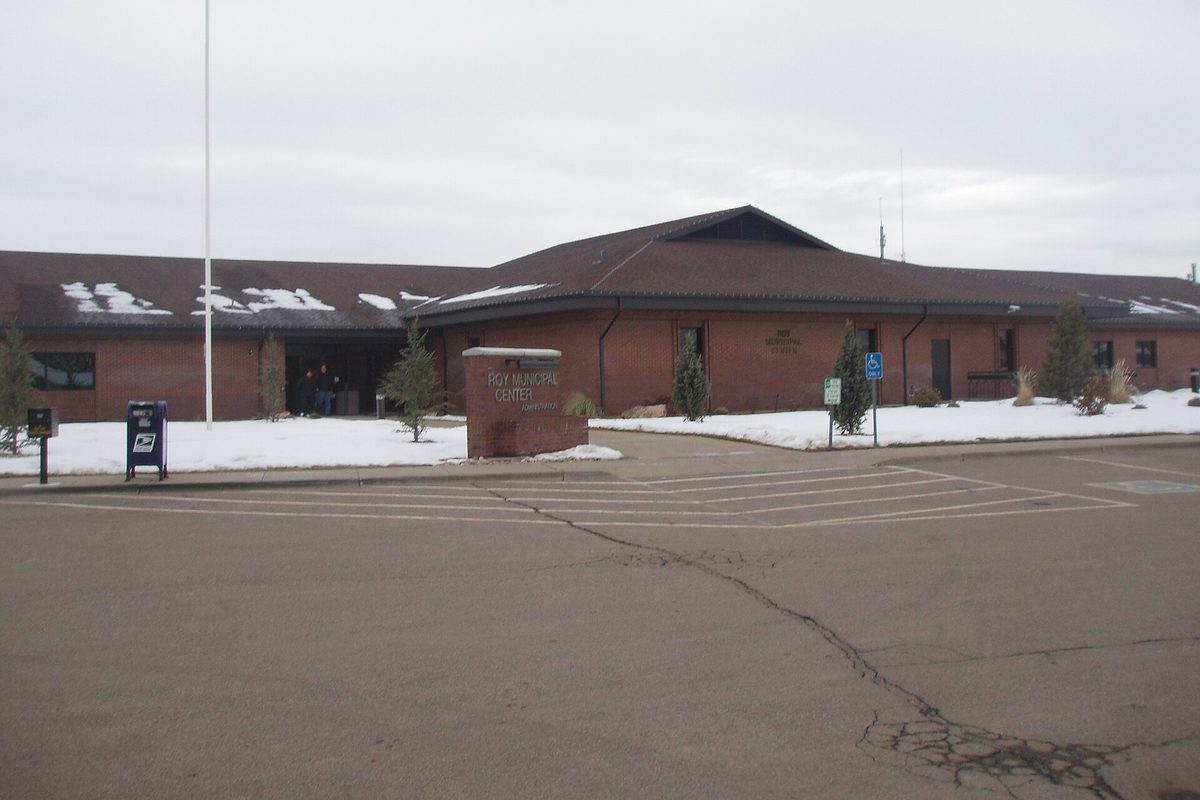 The low brick Roy Municipal Center with a brown roof, snow on the lawns and a mailbox by the curb, under a gray winter sky