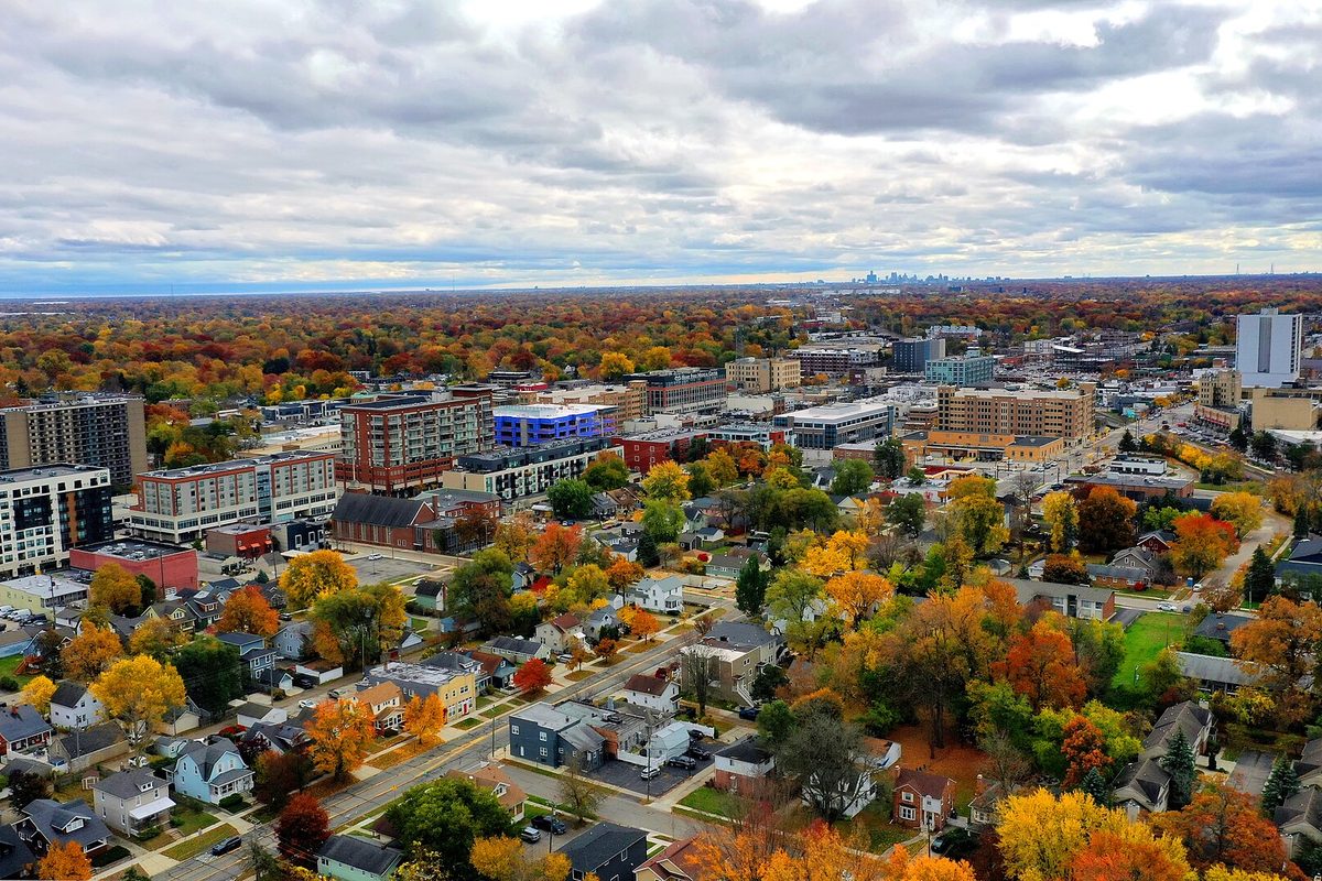 Aerial view of downtown Royal Oak in autumn, apartment blocks and homes among orange and yellow trees, with the Detroit skyline on the horizon