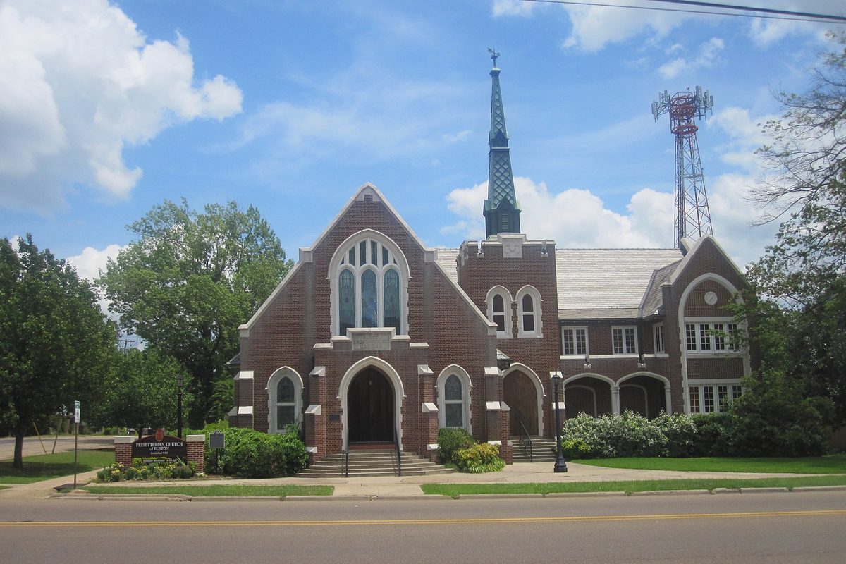 The red brick Presbyterian Church of Ruston, with arched windows and a tall green spire, under a blue sky with white clouds