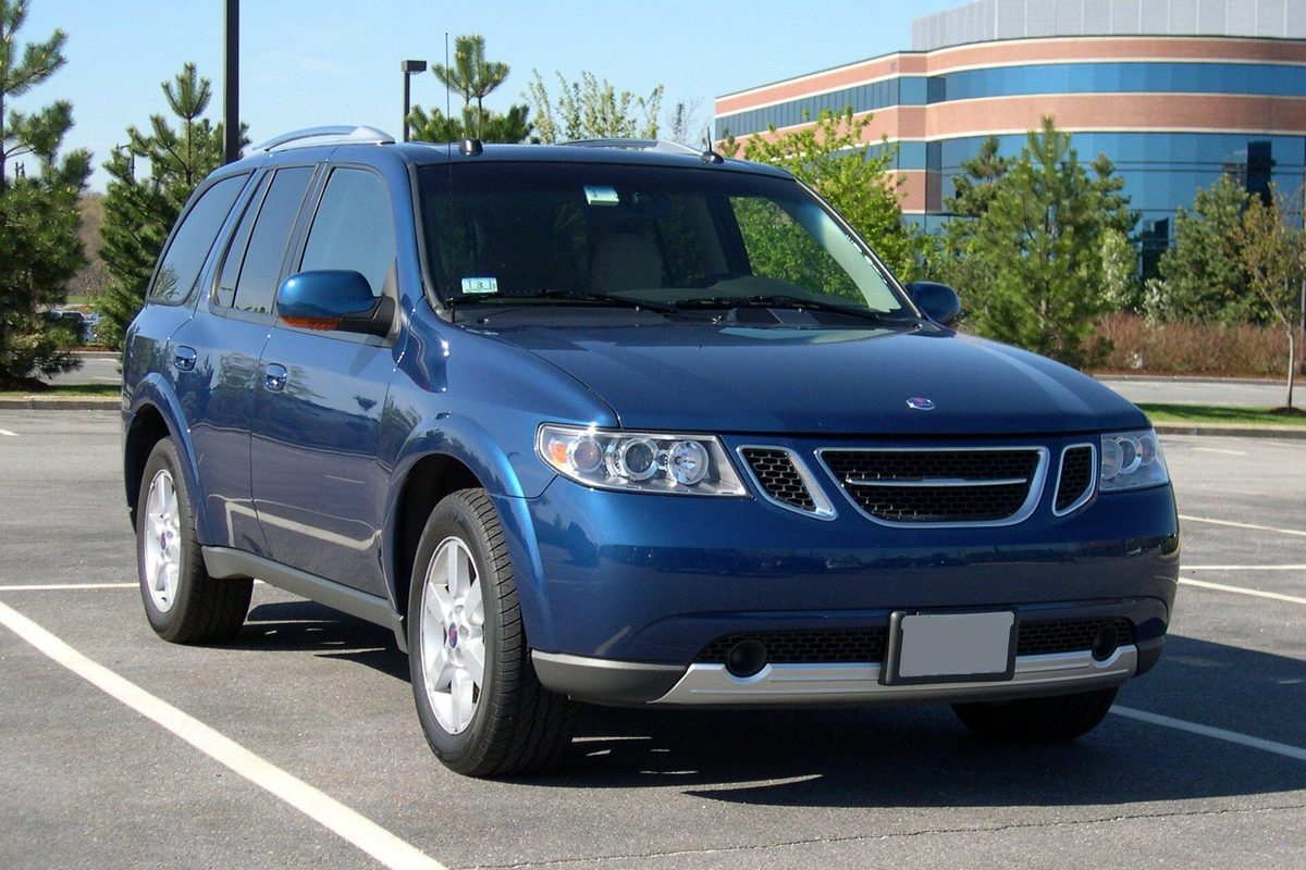 A blue Saab 9-7X SUV parked in an empty lot in front of a curved glass office building