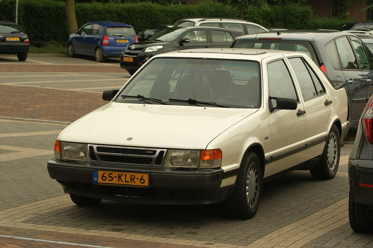 An off-white early Saab 9000 hatchback with the upright front end, parked in a brick-paved lot