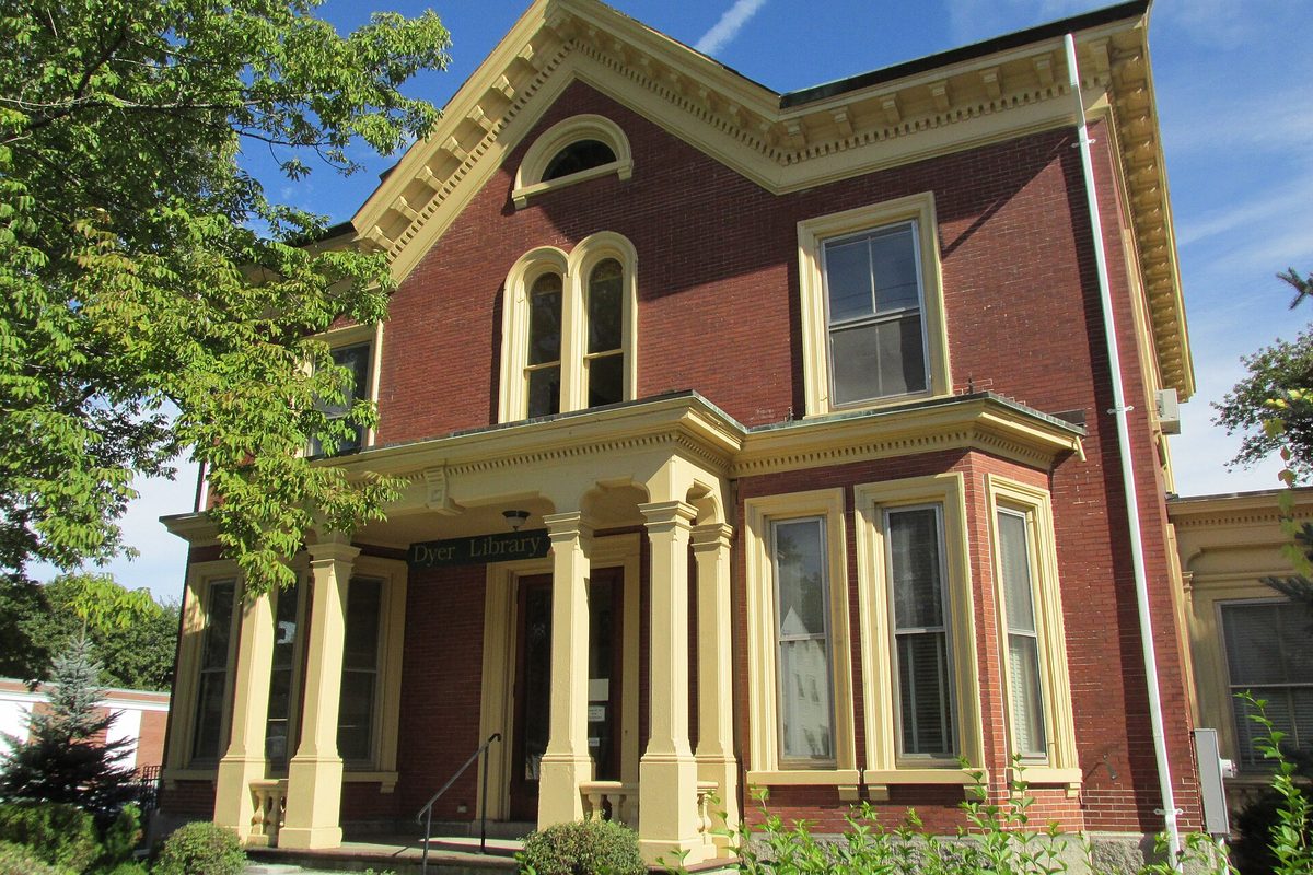 The J.G. Deering House in Saco, a red brick house with yellow trim and a columned front porch under a Dyer Library sign
