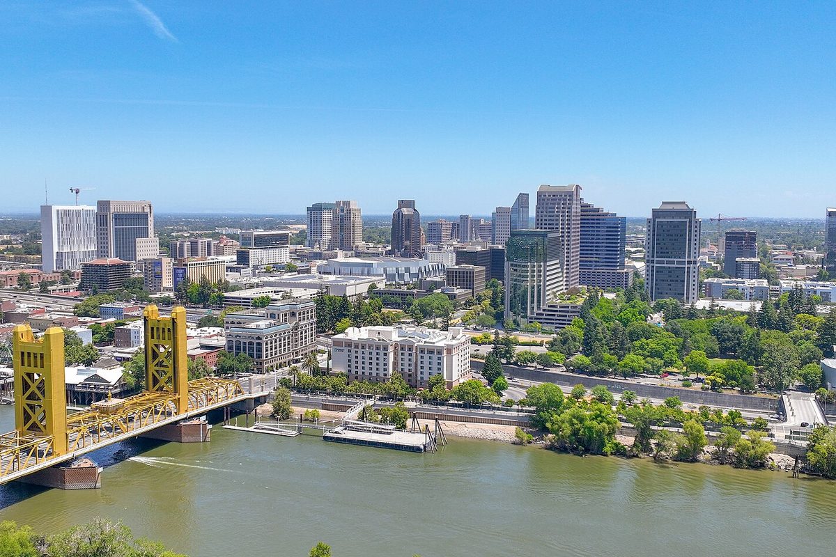 Downtown Sacramento's office towers rising behind a gold-painted lift bridge over the Sacramento River on a clear day
