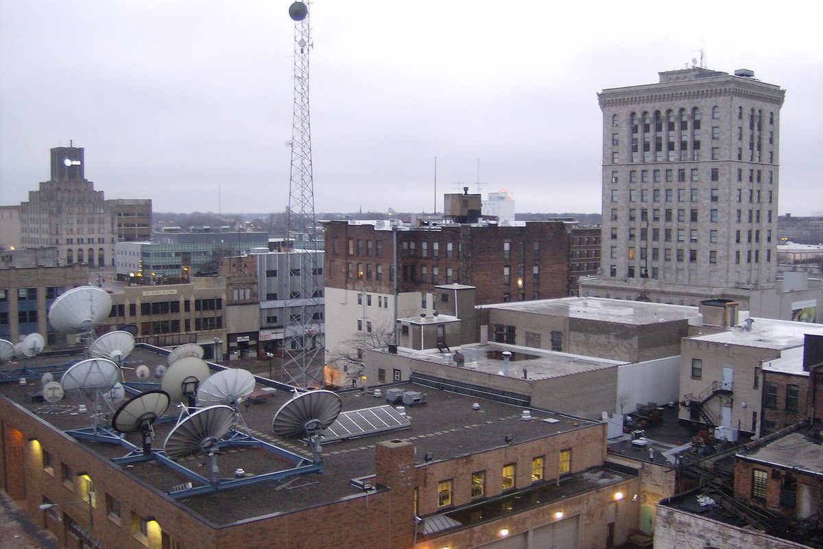 Downtown Saginaw rooftops under a gray sky, satellite dishes on a brick building, a lattice radio tower and a tall stone office building