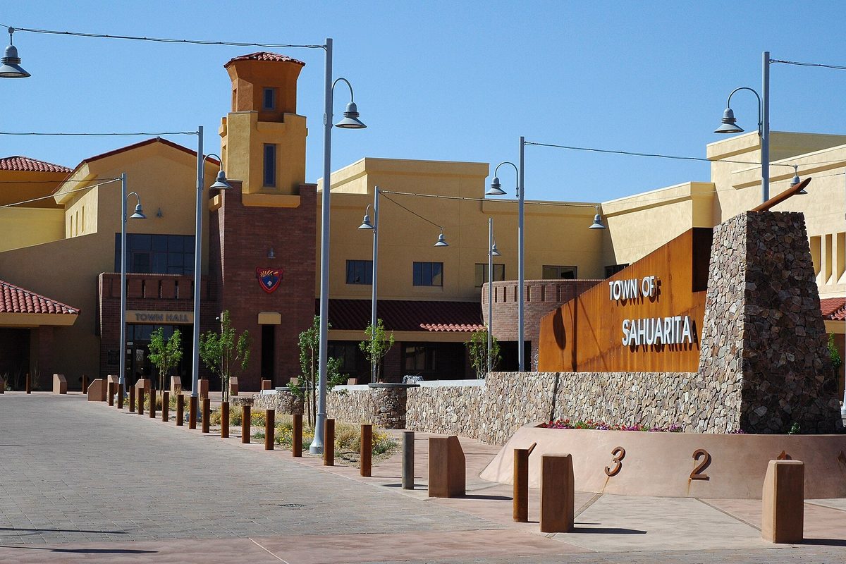 Sahuarita Town Hall, a tan building with a tile-roofed tower, beside a stone and rust-colored Town of Sahuarita sign and a row of street lamps