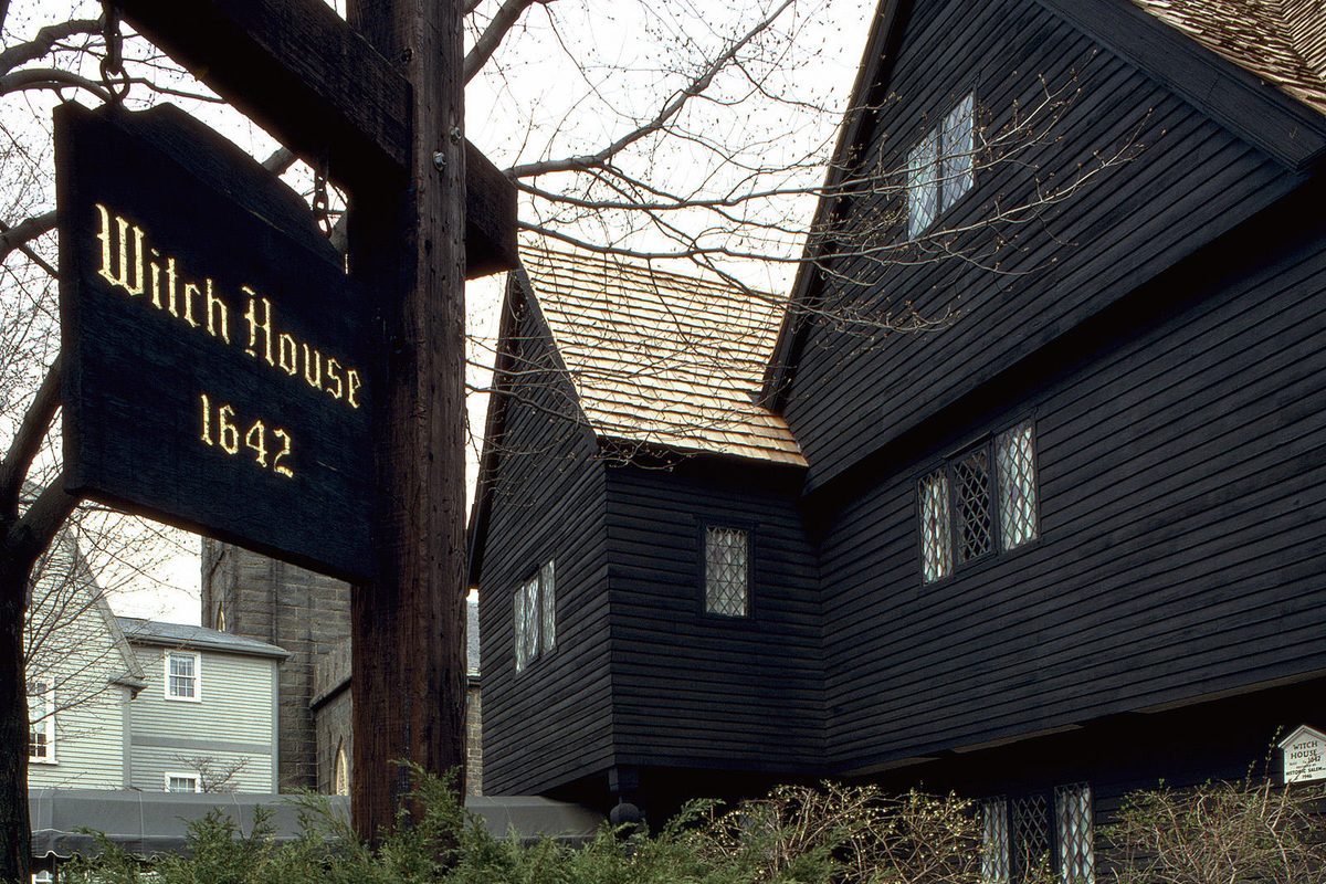 The Witch House in Salem, a dark wooden colonial house with diamond-paned windows, behind a hanging sign reading Witch House 1642