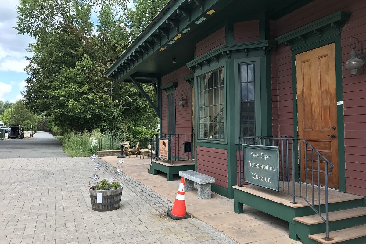 The Salem Depot Transportation Museum, a small red wooden depot with green trim and a green sign, beside a brick plaza and a tree-lined path
