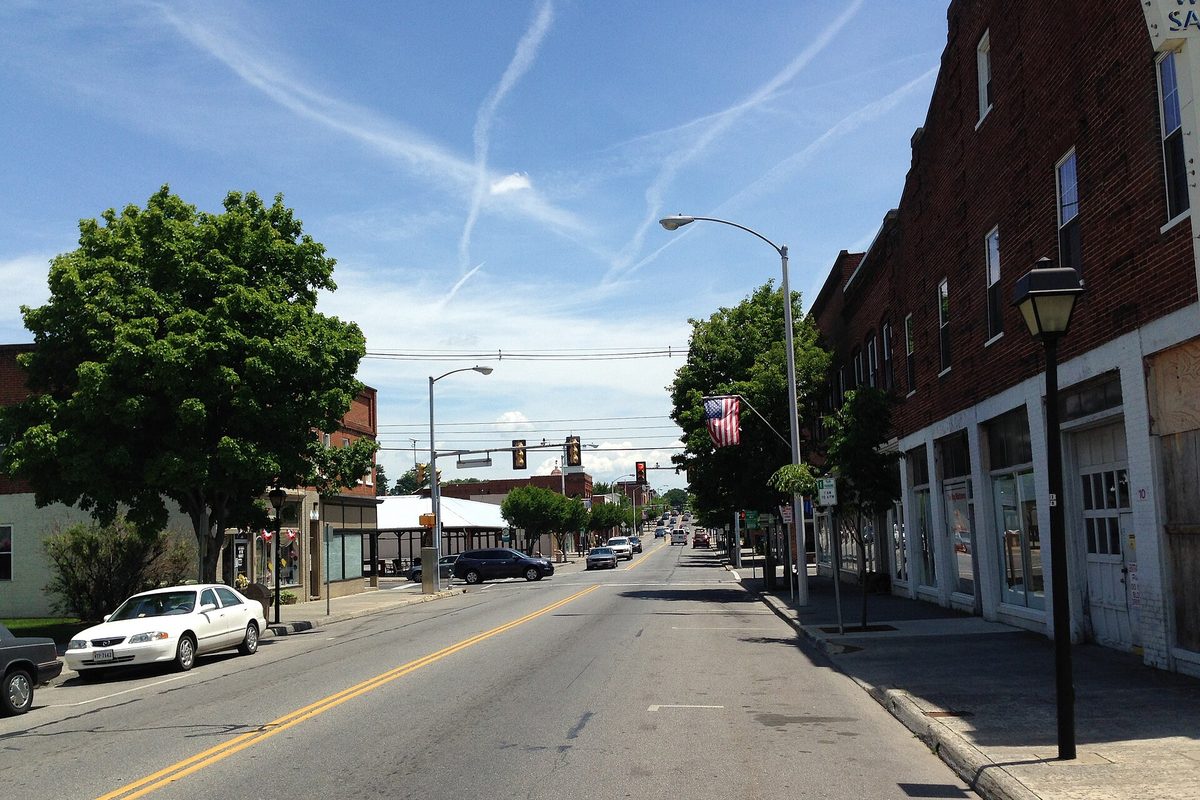Main Street in Salem on a sunny day: brick storefronts with an American flag on the right, parked cars at the curb, and a traffic light down the road