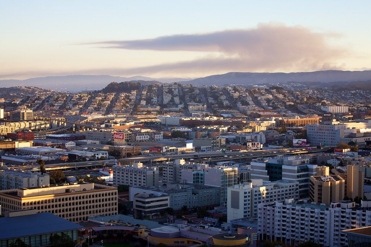 Hillside rows of houses and city blocks at dusk with a long plume of smoke on the horizon, taken on the evening of the 2010 San Bruno fire
