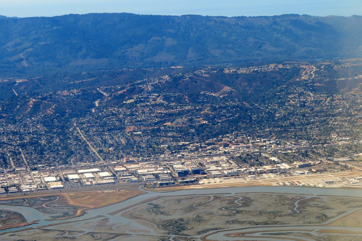 Aerial view of San Carlos, with business parks beside the bay marshes in front and homes climbing the wooded hills behind