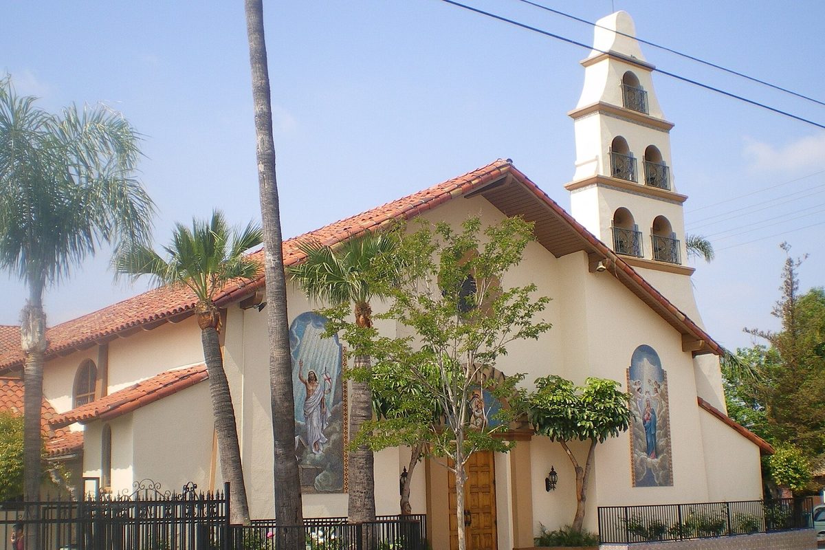 Santa Rosa Catholic Church in San Fernando, a white stucco church with a red tile roof, a tiered bell tower and painted saints by the door, framed by palm trees
