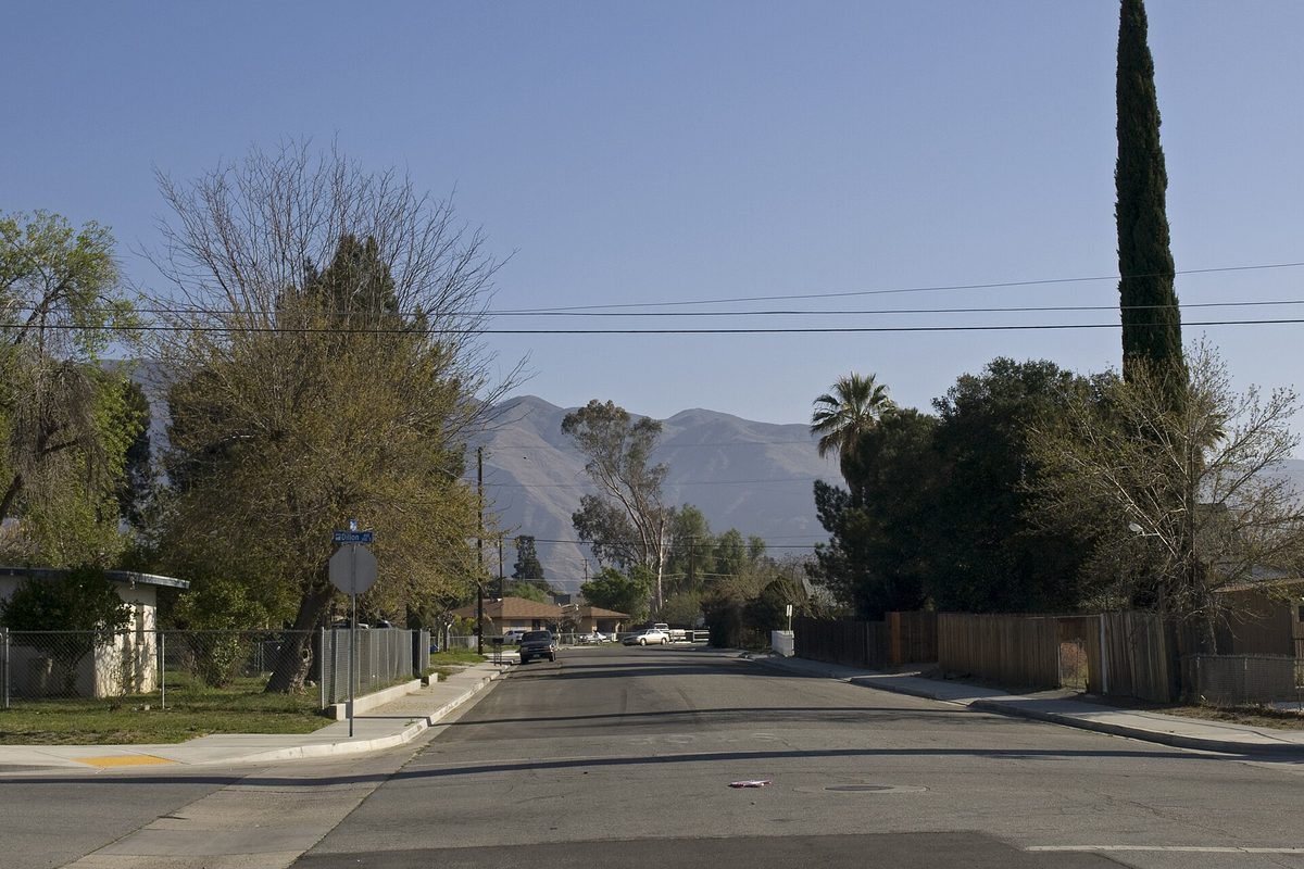 A quiet stretch of West Ash Street in San Jacinto with fenced yards, a tall cypress and a palm, and bare mountains beyond
