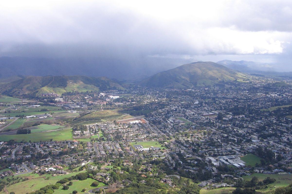 View from Bishop Peak over San Luis Obispo's neighborhoods and green hills, with dark rain clouds over the mountains behind