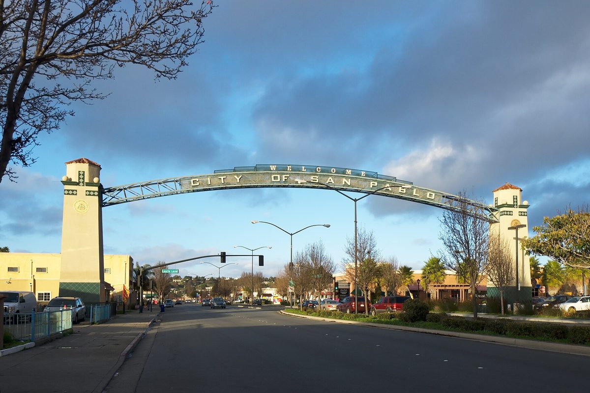 The arched Welcome to the City of San Pablo sign spanning San Pablo Avenue between two towers, under a cloudy sky