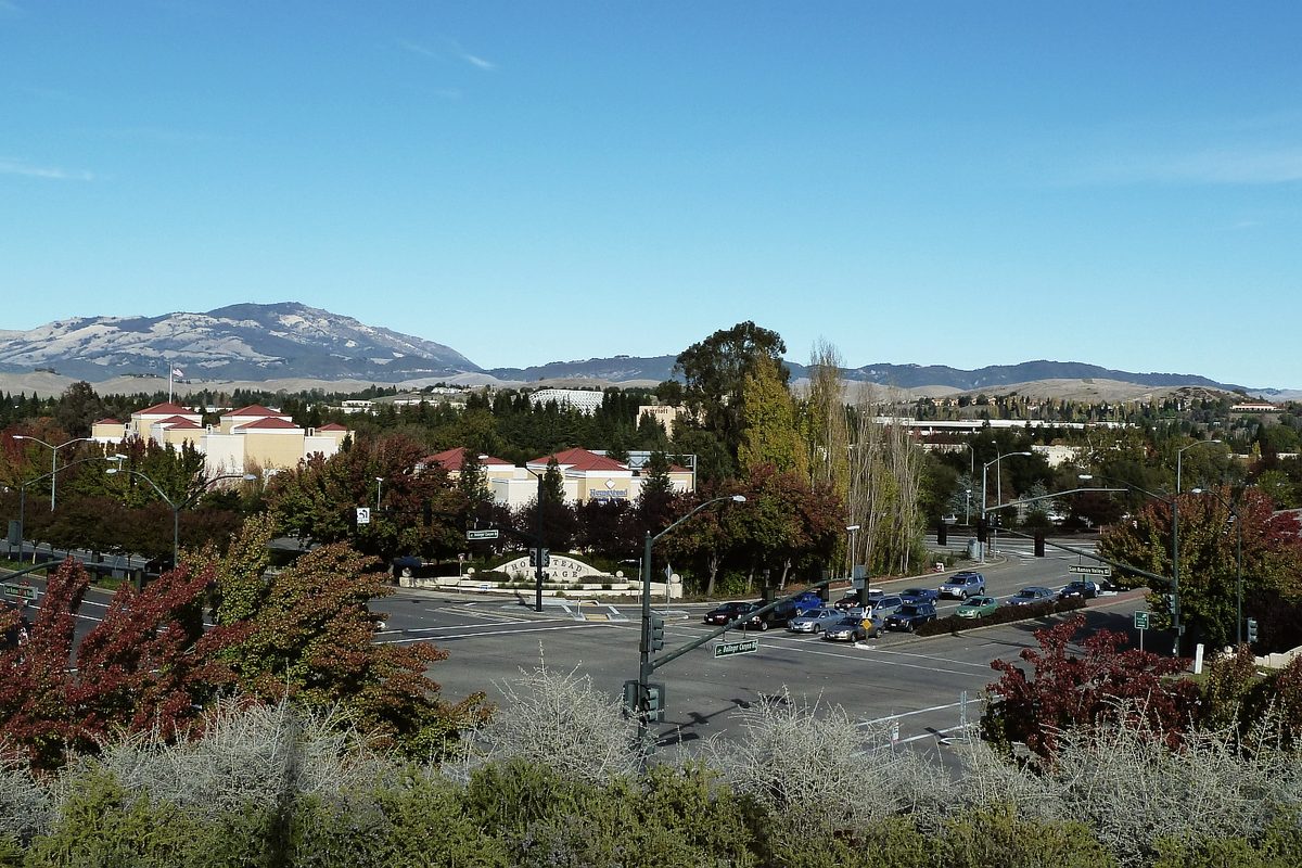 San Ramon seen from Memorial Park in late autumn: a signalized intersection with parked cars, red-roofed buildings and a dusted mountain ridge under clear blue sky