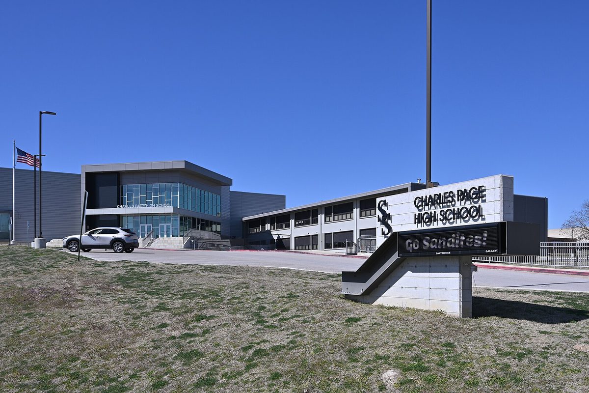 The Charles Page High School sign reading Go Sandites in front of the school's modern gray building in Sand Springs, with a white SUV parked out front