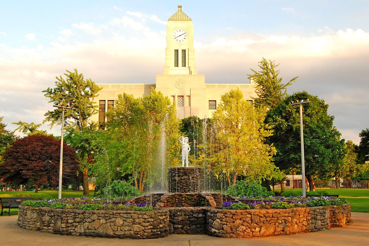 The Boy with the Boot statue in its fountain in front of the Erie County Courthouse clock tower in Sandusky, ringed by a low stone wall and flower beds