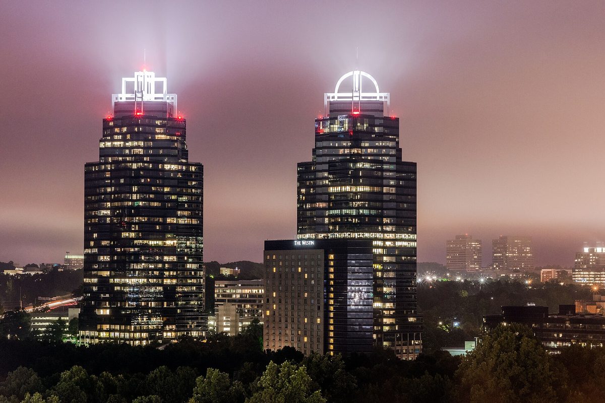 The King and Queen towers of Concourse Corporate Center in Sandy Springs lit up at night, their crowns glowing through low fog above dark trees