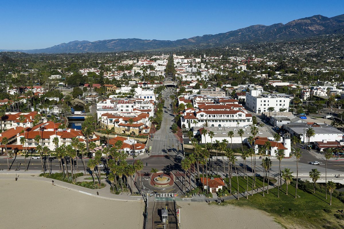 Aerial view of downtown Santa Barbara, with red-tile roofs and a palm-lined street running from a beachfront roundabout toward the mountains