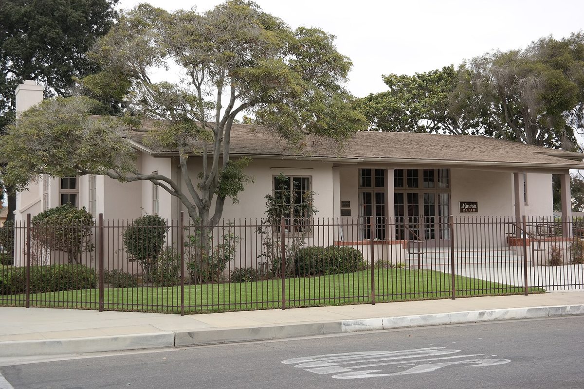 The Minerva Club of Santa Maria, a low stucco building with a wide porch behind a black iron fence and old trees