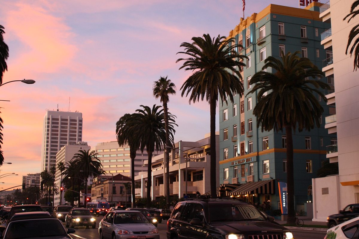 Ocean Avenue in Santa Monica at sunset, tall palms and a teal hotel above a line of cars with their headlights on