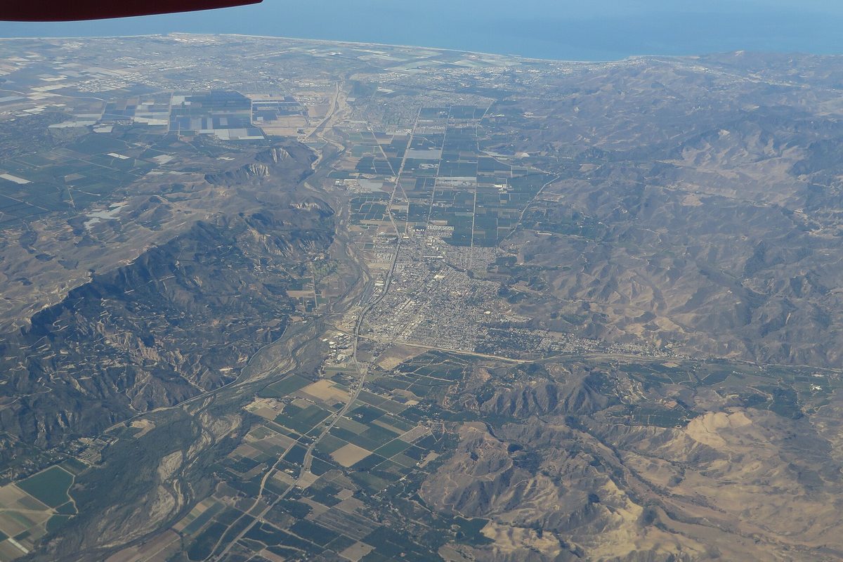Aerial view of Santa Paula in a narrow valley, the town grid surrounded by farm fields and dry hills, with the ocean on the horizon