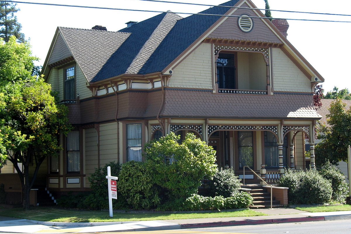 The two-story Victorian Cnopius House on College Avenue in Santa Rosa, painted in browns and cream, with shrubs and a sign in the front yard