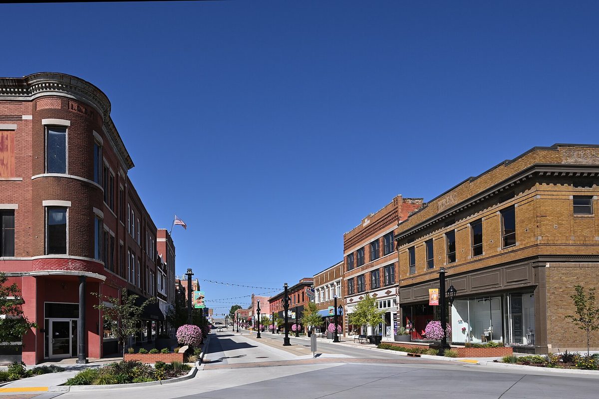 Brick storefronts on Dewey Avenue, Route 66, at Park Street in Sapulpa, with the rounded corner of the Odd Fellows Building on the left and flower planters along the sidewalk