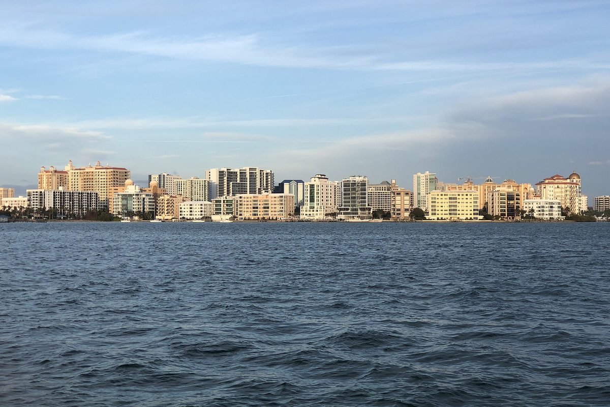 The Sarasota skyline of pale high-rise buildings seen across choppy blue bay water under a wide sky