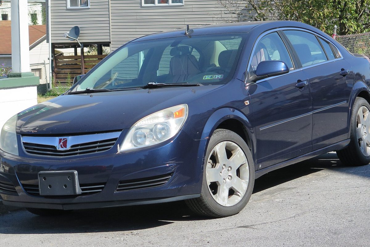 A dark blue 2008 Saturn Aura sedan parked on a residential street with houses behind it