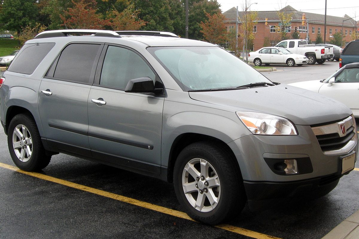 A gray Saturn Outlook crossover parked in a wet lot, its front wheels over a yellow painted line