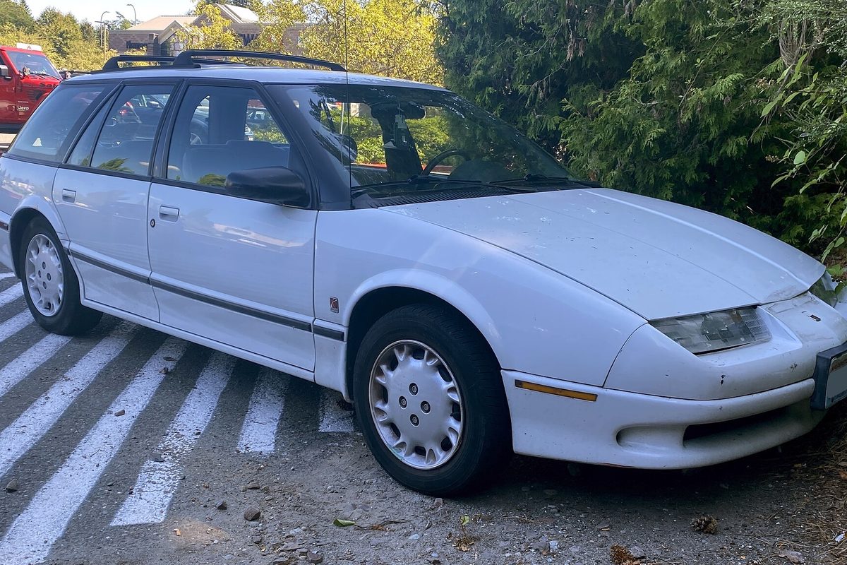 A white 1995 Saturn SW2 station wagon with a roof rack and plastic wheel covers, parked over faded white parking stripes